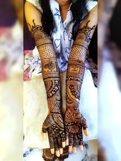 A full-arm bridal design with a mix of patterns. It includes a doli (palanquin) motif and the couple's names, surrounded by intricate floral and geometric work.