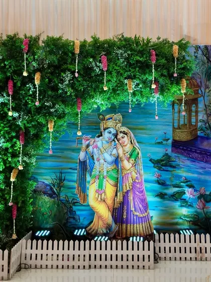 A Radha-Krishna themed photo corner we created for a baby shower at Hiravati Hall. The divine couple is set against a lush green foliage wall with delicate hanging floral tassels, creating a perfect photo opportunity.