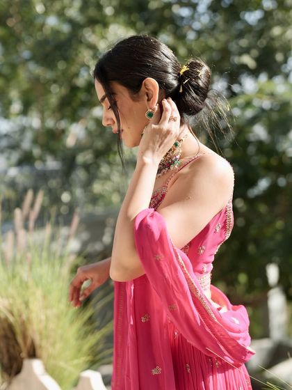 A side profile highlighting the elegant hairstyle and jewelry paired with the pink lehenga, showing how to style a complete festive look.