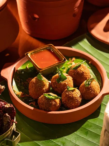 Crispy fried appetizer balls served in a rustic terracotta bowl. The natural materials and lighting give it an earthy feel.