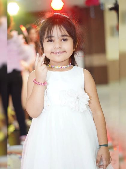 A young girl in a simple white dress smiles for the camera at a party. We capture beautiful, natural portraits of children enjoying the celebration.