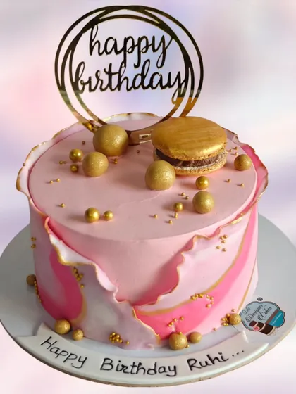 A fault line cake in pink and gold, topped with a macaron. This modern design technique creates a beautiful and unique look.