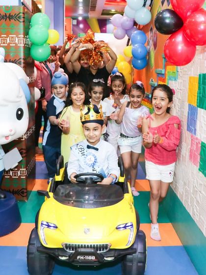 The birthday boy being cheered on by his friends as he makes his grand entrance in a toy car. It's a moment of pure joy and excitement.