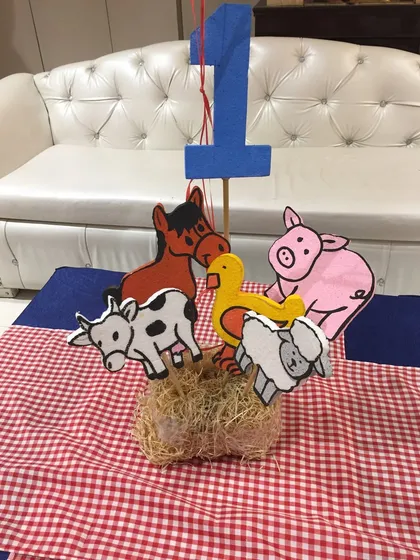 A DIY-style farm animal centerpiece for a jungle or farm-themed party, featuring cute animal cutouts on a hay bale.