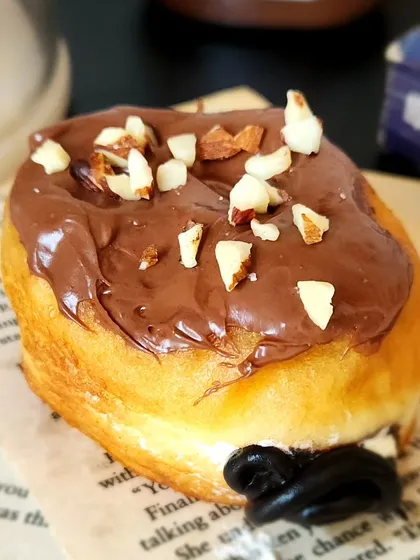 A close up of our Nutella Almond Crunch Donut. This soft donut is generously topped with Nutella and crunchy almonds, a perfect sweet indulgence for a mid day office break.