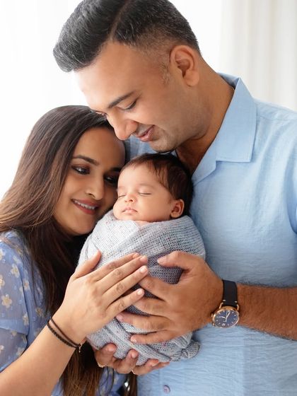 A beautiful portrait of new parents, holding their swaddled baby close. Their love and happiness are radiant.