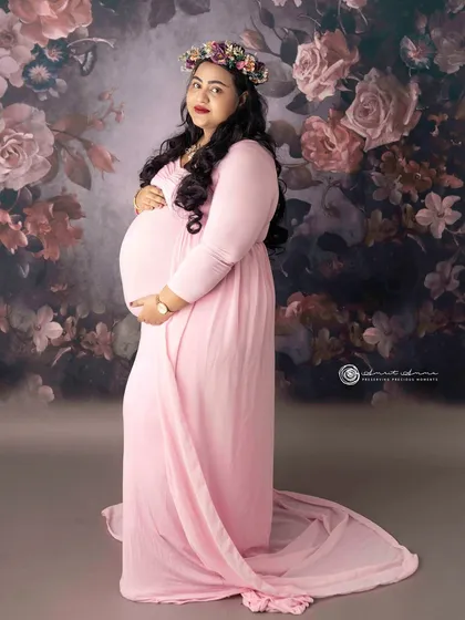 A classic pose against a floral backdrop. The flowing pink gown and flower crown create a soft, romantic feel, celebrating the beauty and femininity of pregnancy.