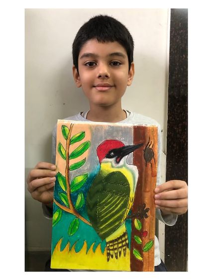 A student proudly presents his detailed woodpecker drawing. We study animals and birds to learn about their shapes, colours, and features, which improves our drawing skills.