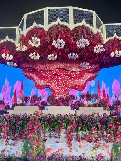 A full view of the surreal stage, with its massive floral ceiling installation, LED backdrop, and a foreground of lush purple flowers.