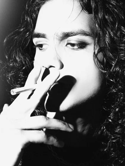 An intimate close-up of the model smoking, captured in high-contrast black and white. The focus is on the details: the smoke, the light, and the model's expression.