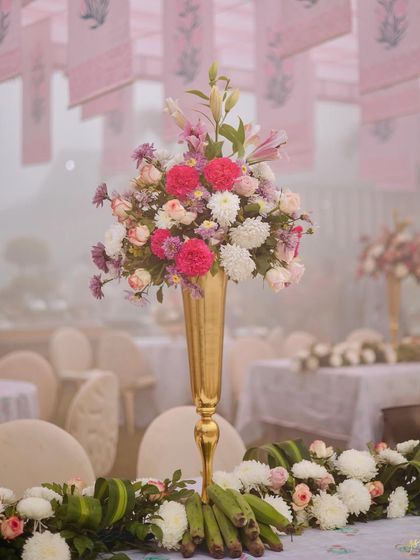 A tall, elegant floral centerpiece in a golden vase, featuring a mix of pink and white flowers, adding a touch of romance to the table setting.