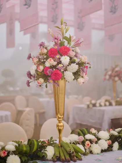 A tall, elegant floral centerpiece in a golden vase, featuring a mix of pink and white flowers, adding a touch of romance to the table setting.