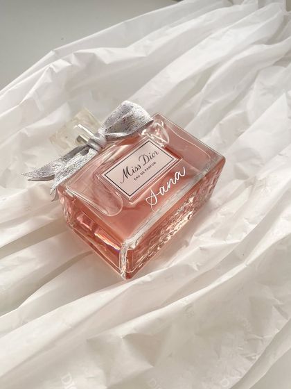 A personalized Miss Dior bottle, resting on soft fabric. This image captures the romantic and timeless appeal of a custom-engraved fragrance.