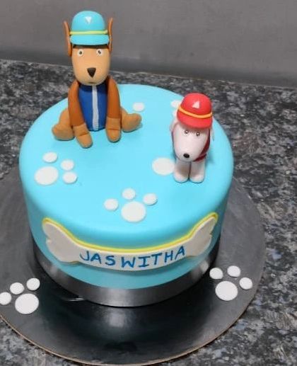 A cute and simple PAW Patrol cake with fondant figures of the heroic pups. The design includes paw prints and a bone-shaped name plaque for a personalized touch.