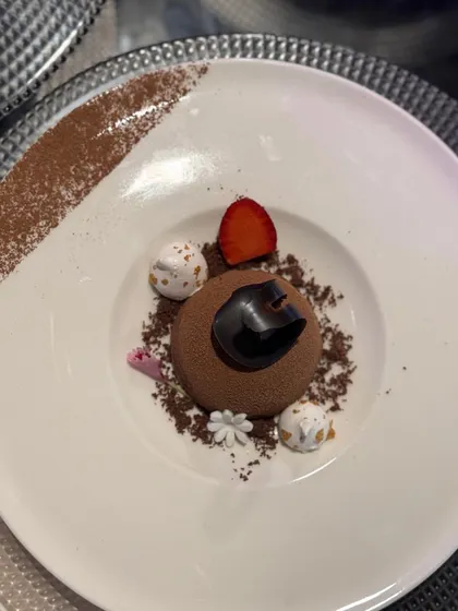 A perfect chocolate dome dessert, dusted with cocoa powder and surrounded by meringue kisses and a single strawberry slice. Pure indulgence.
