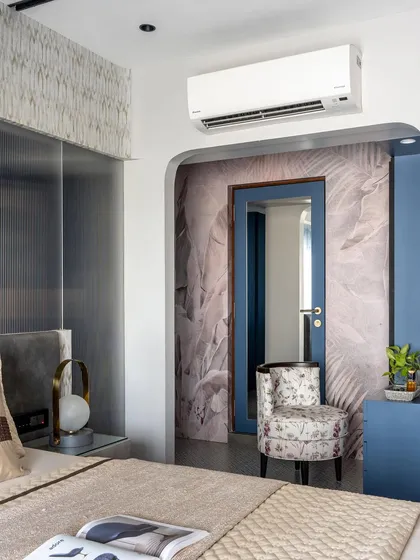 An arched entryway leads to the walk-in closet in this master bedroom. The feather-print wallpaper and floral chair add a touch of softness and personality.