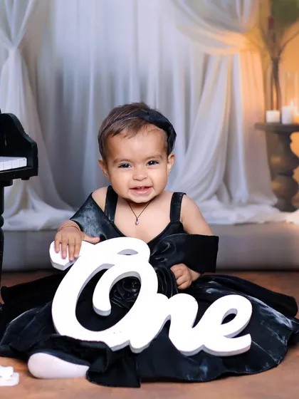 A happy one-year-old girl holding a 'One' sign during her elegant piano-themed birthday shoot.