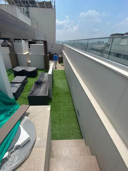 A long view of a narrow terrace space transformed with a strip of artificial grass, providing a green walkway alongside modern outdoor lounge furniture.
