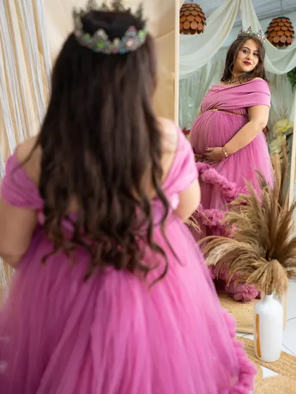 A creative mirror shot. The mom-to-be, in a pink gown and crown, looks at her reflection, creating a thoughtful and artistic portrait about her journey into motherhood.