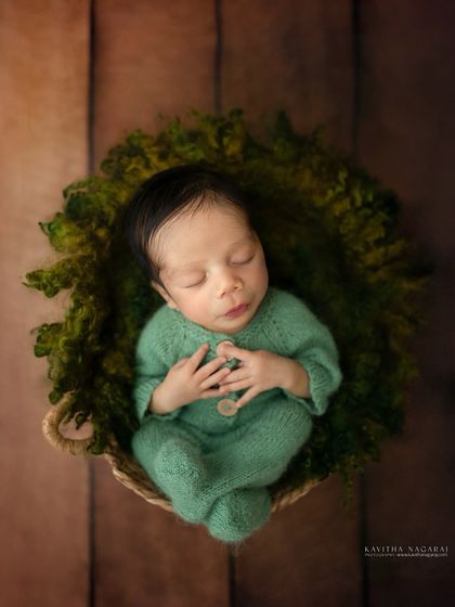Three-week-old Abir sleeps peacefully in a mossy green basket. The overhead view and natural textures create a beautiful, earthy feel.