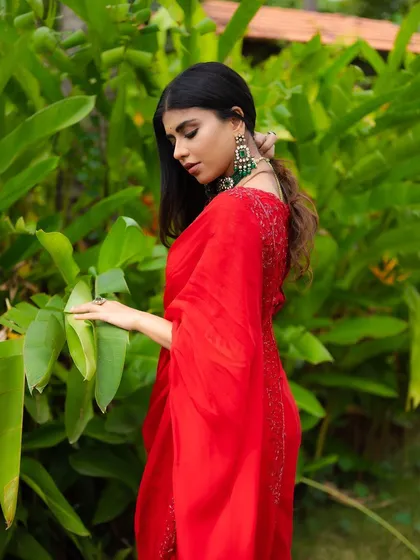A portrait of a model in a red saree, looking back over her shoulder. The vibrant green background provides a beautiful contrast, making the red fabric stand out.