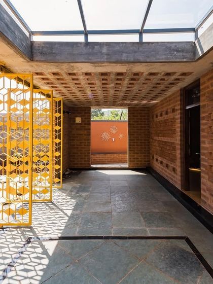 A corridor in the Good Bricks Company office, where sunlight filters through yellow, geometric screens and a skylight. The play of light and shadow on the stone floor and brick walls is a key part of the design experience.
