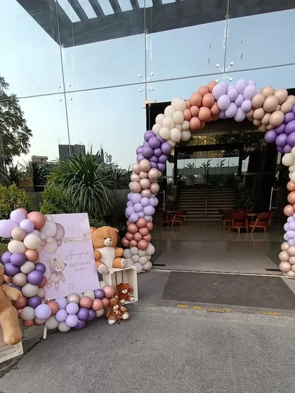 A welcoming entrance for a teddy bear themed party. The balloon arch in muted tones of purple, brown, and beige, combined with the welcome sign and plush bears, creates a warm and inviting atmosphere.