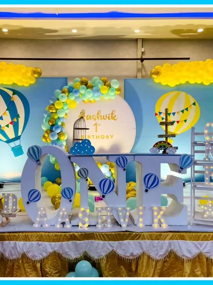A dreamy hot air balloon-themed first birthday. The stage is set with a large 'ONE' marquee table, a teddy bear in a balloon-basket, and a sky-blue backdrop.