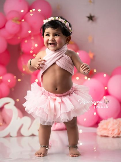 Standing tall and proud at one year old. This photo captures the exciting milestone of learning to stand, surrounded by a fun birthday setup.