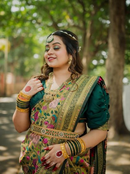 A candid portrait of the bride with a gentle, happy expression. The natural light beautifully illuminates her features and the rich details of her saree.