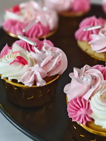 A close-up of my vanilla cupcakes with swirls of pink and white strawberry buttercream. I finish them with little edible pearls and hearts to make them perfect for any happy occasion.