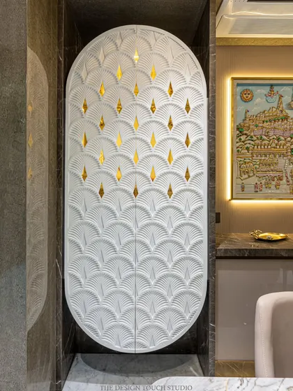 This elegant, space-saving mandir is concealed within a custom Corian cabinet. The oval-shaped doors feature a beautiful carved pattern with golden inlays that glow when the mandir is lit from within.