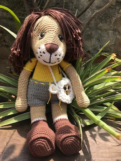 Jireh the lion sitting amongst the plants. He's a large and huggable doll, perfect for storytelling and imaginative play.