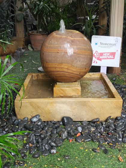 The Rainbow Sandstone sphere fountain, shown here with water bubbling from the top. The square tank provides a stable base and a modern aesthetic.