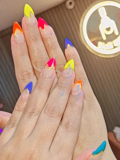 A multi-colored French manicure with sharp, v-shaped tips in vibrant shades of yellow, pink, blue, and orange. This geometric and colorful style is modern and full of energy.