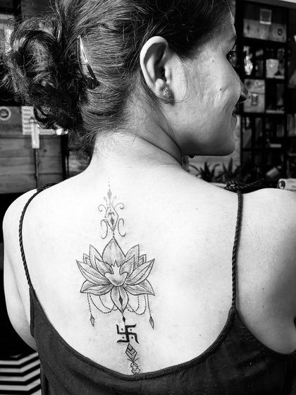This elegant backpiece combines the sacred lotus flower with a swastika, symbols of purity, enlightenment, and good fortune. It's a beautiful example of a spiritual spine tattoo.