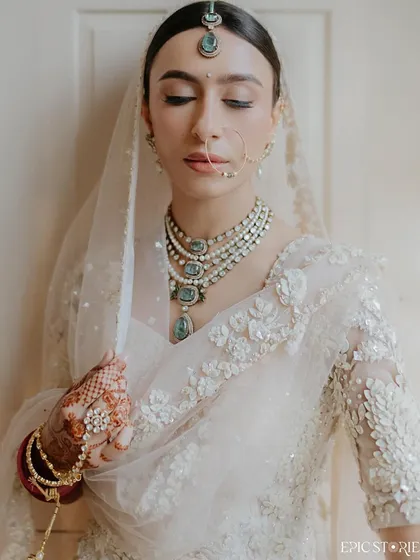A close-up portrait focusing on the bride's serene expression and exquisite jewelry. This shot highlights the delicate details that complete the bridal look, from the nath to the layered necklace.