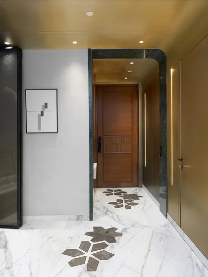 The entryway of this New Delhi residence sets a tone of refined elegance. The design features warm brass paneling, a concealed door for a seamless look, and custom marble flooring with geometric inlays. An arched pooja alcove is integrated into the design, blending spiritual serenity with modern aesthetics.