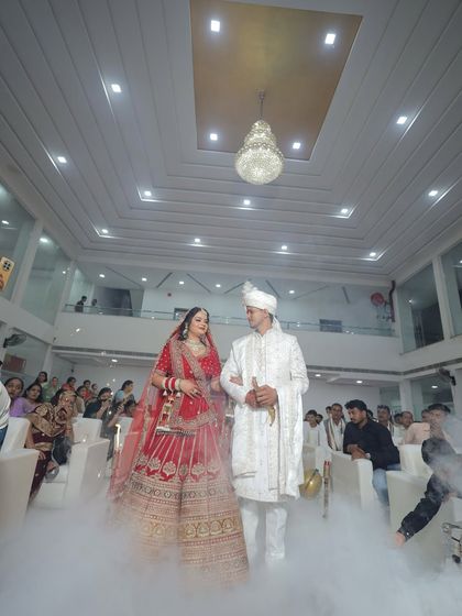 A grand entrance with the bride and groom walking through theatrical smoke. The bride's red lehenga and makeup look absolutely stunning.