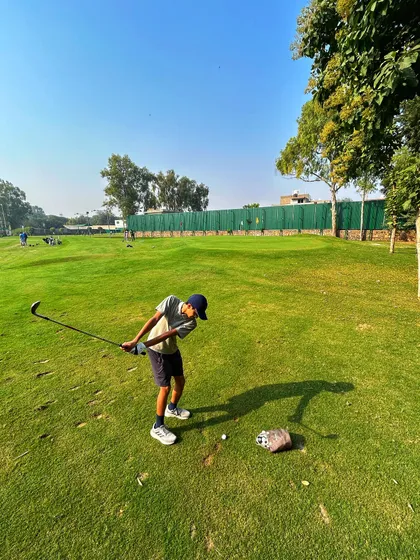 A young golfer practices his chipping on a sunny day, showing great concentration.