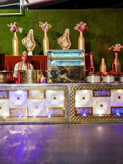 An elaborate white and gold catering counter, complete with a refrigerated display for desserts and traditional staff attire.