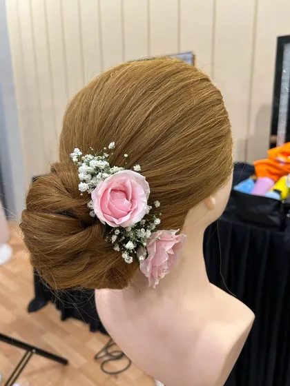 A classic floral bun is a timeless choice for any bride. Here is a practice shot on a mannequin, showing the intricate placement of fresh roses and baby's breath in a traditional updo.