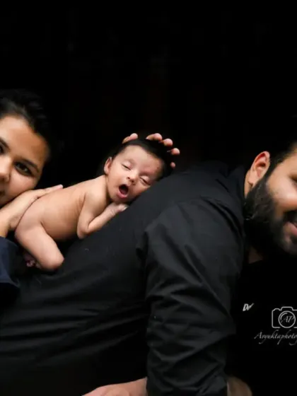A beautiful family portrait with a newborn. The baby is sleeping soundly on their father's back, showing a moment of trust and connection.