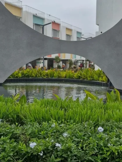 The same water feature by day, showing how the concrete sculpture acts as a modern art piece within the landscape. The surrounding greenery and calm water provide a tranquil atmosphere in this residential development.