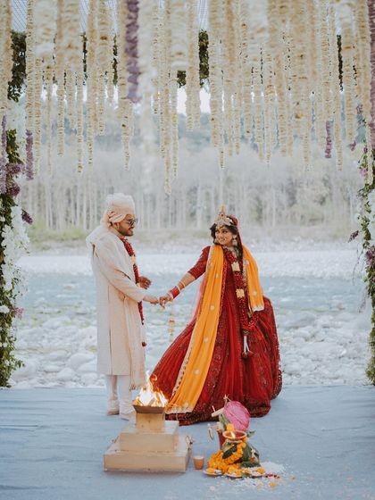 A breathtaking Hindu wedding ceremony by the river. The couple takes their pheras around the holy fire, framed by a stunning floral mandap and the natural landscape.