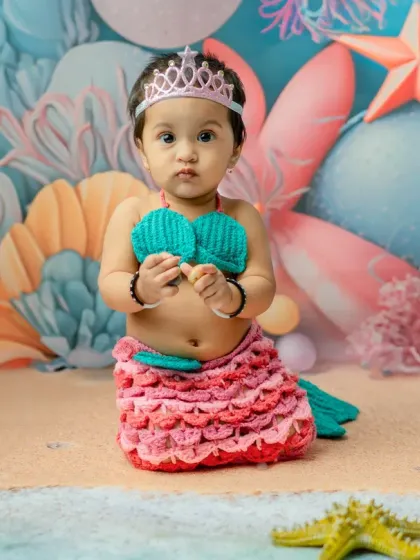 A direct and engaging portrait of the baby mermaid. The details of the set, like the paper flowers and starfish, add texture and depth to the image.