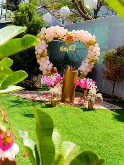 A glimpse through the leaves at a sweet garden proposal scene. The heart-shaped balloon arch stands as the centerpiece, surrounded by lush greenery, creating a feeling of a private, secret garden.