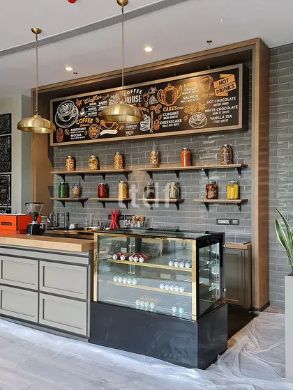 The cafe at the Sheraton beckons with an understated allure. A brick-tiled backdrop in grey undertones combines with warm wooden textures and subtle metallic hints, creating an inviting space where modern comfort meets rustic sophistication.