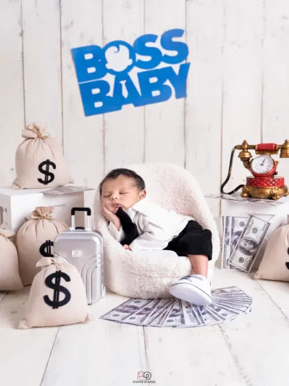 A series from a 'Boss Baby' themed newborn shoot. The setup includes a tiny armchair, a miniature briefcase, and prop money, creating a playful and humorous scene for a baby boy's first portraits.
