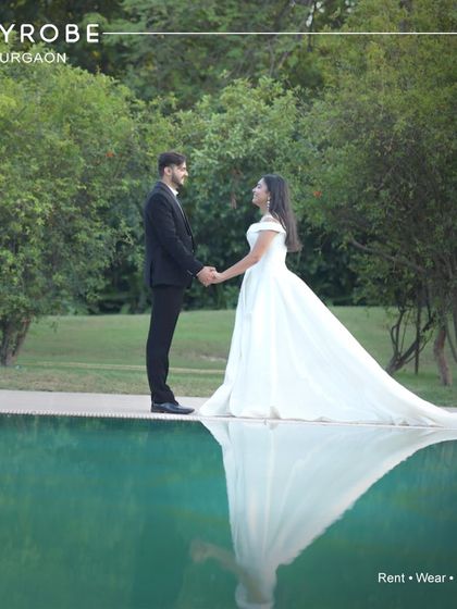 A fairytale moment by the water. Her pristine white trail gown and his classic black suit create a timeless, cinematic look that is perfect for a pre-wedding photoshoot.